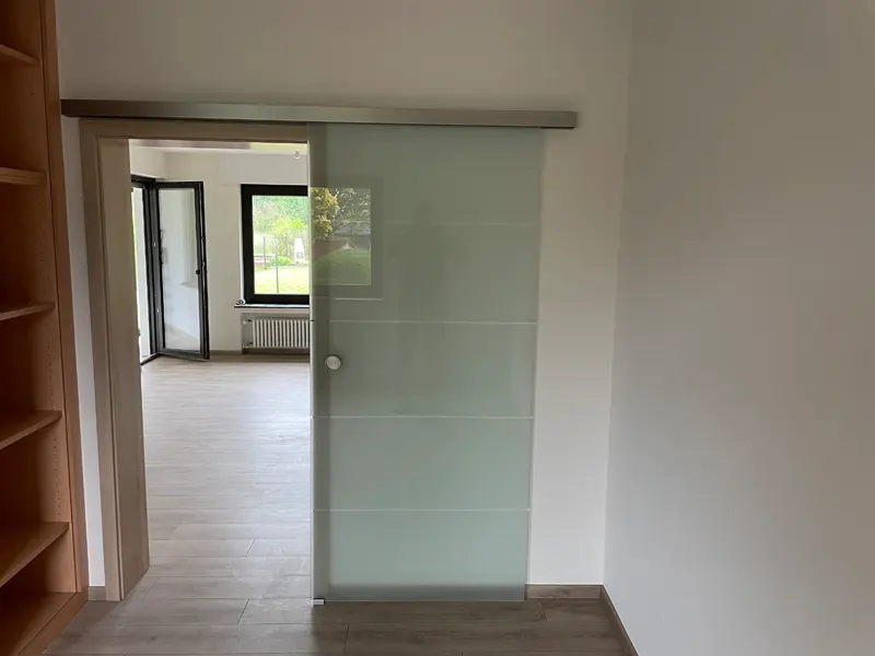 Vor der Wand laufende Glasschiebetür mit matter Oberfläche und waagerechten klaren Streifen