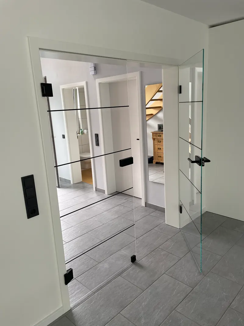 Zwei klare Innentüren aus Glas mit schwarzen Beschlägen und waagerechten schwarzen Linien