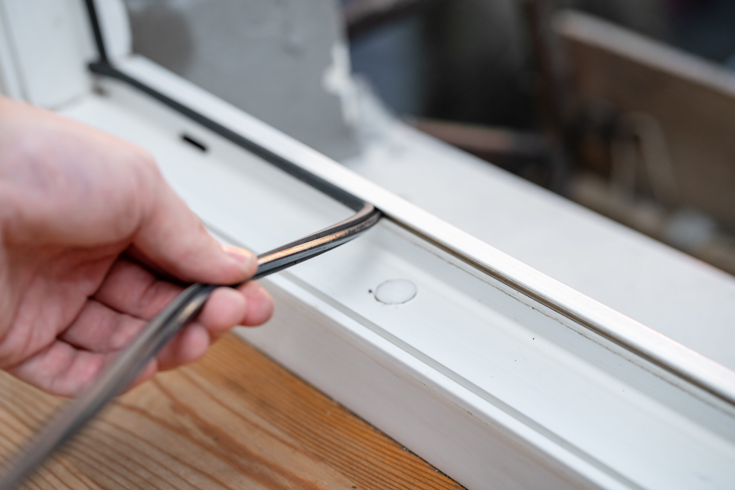 Hand setzt eine Gummidichtung in einen weißen Fensterrahmen ein.